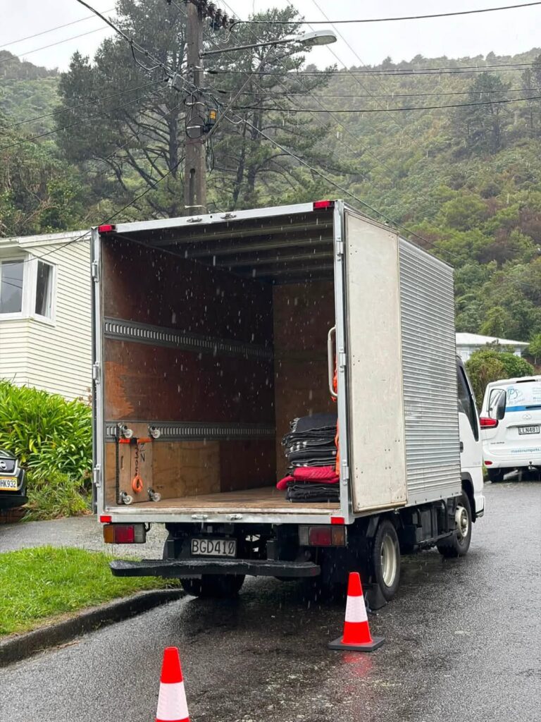 Moving truck with furniture blankets and tie rails, ready to load on a rainy Wellington street